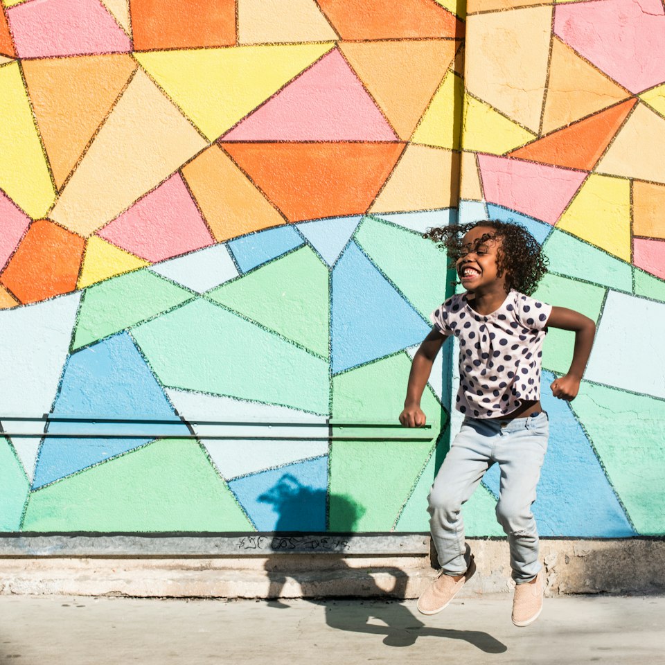 A smiling child jjumping, with a colourful backgrounf behind.